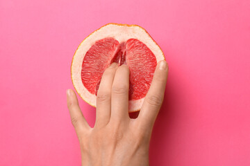 Woman touching half of grapefruit on pink background, top view. Sex concept - obrazy, fototapety, plakaty