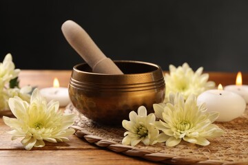 Tibetan singing bowl with mallet, beautiful chrysanthemum flowers and burning candles on wooden...