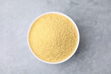 Raw couscous in bowl on gray table, top view