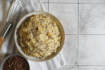 Chocolate chip cookie dough in bowl and metal whisk on tiled textured table, top view. Space for text