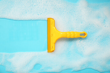 Squeegee with detergent and foam on blue background