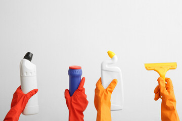 Female hands in rubber gloves holding cleaning supplies on beige background