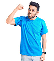 Young handsome man with beard wearing casual t-shirt angry and mad raising fist frustrated and furious while shouting with anger. rage and aggressive concept.