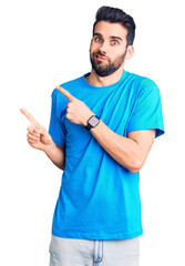 Young handsome man with beard wearing casual t-shirt pointing aside worried and nervous with both...