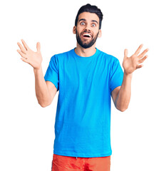 Young handsome man with beard wearing casual t-shirt celebrating victory with happy smile and winner expression with raised hands