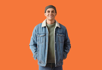 Young man in winter clothes on orange background