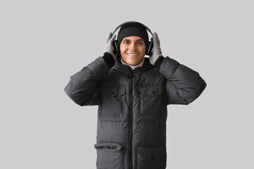 Young man in puffer jacket with headphones on light background