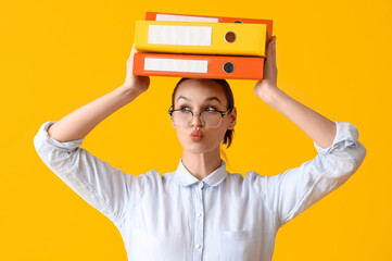 Thoughtful young businesswoman with document folders on yellow background