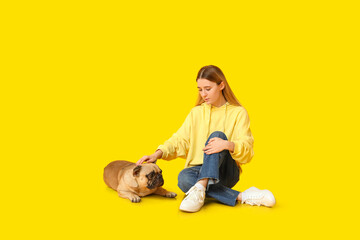 Beautiful young woman with cute pug dog sitting on yellow background