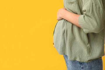 Pregnant woman on yellow background, closeup