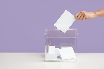 Hand putting voting paper in ballot box on lilac background