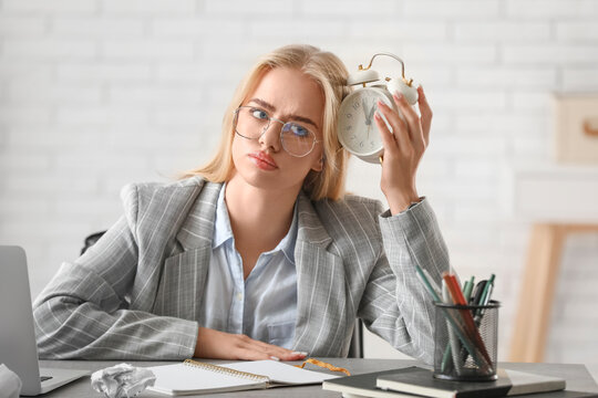 Young thoughtful businesswoman with alarm clock trying to meet deadline in office. Time management concept