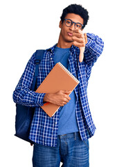 Young african american man wearing student backpack holding book looking unhappy and angry showing rejection and negative with thumbs down gesture. bad expression.