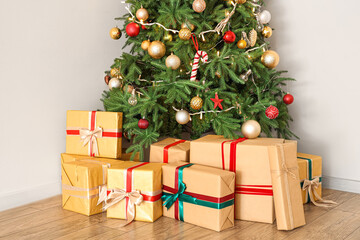 Fototapeta na wymiar Glowing Christmas tree with presents near light wall in room