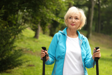 Senior woman with Nordic walking poles outdoors, space for text