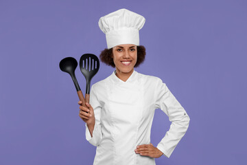 Happy female chef in uniform holding skimmer and ladle on purple background