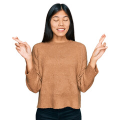 Beautiful young asian woman wearing casual winter sweater gesturing finger crossed smiling with hope and eyes closed. luck and superstitious concept.