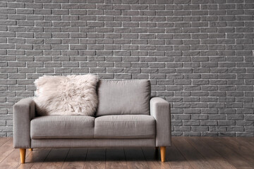 Sofa with fur mat near grey brick wall in room