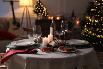 Christmas table setting with burning candles, appetizers and dishware in room