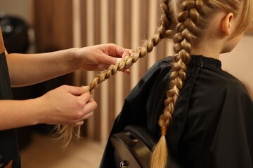 Professional hairdresser braiding girl's hair in beauty salon, closeup - obrazy, fototapety, plakaty