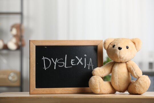 Teddy bear and small blackboard with word Dyslexia on wooden table in room