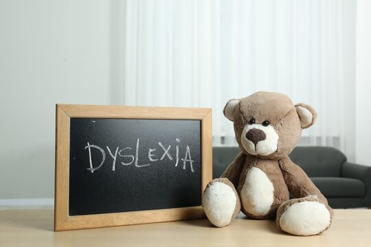 Teddy bear and small blackboard with word Dyslexia on wooden table indoors