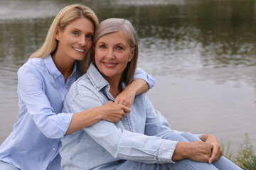 Happy mature mother and her daughter hugging near pond