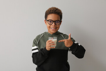 Little African-American boy pointing at glass of milk on white background