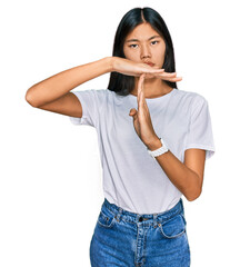 Beautiful young asian woman wearing casual white t shirt doing time out gesture with hands,...