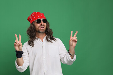 Stylish hippie man in sunglasses showing V-sign on green background