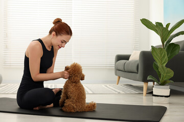 Young woman practicing yoga on mat with her cute dog at home