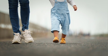 close up leg of infant baby walking on path with mother helping