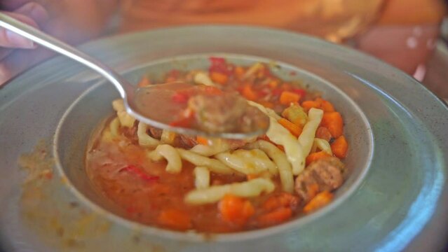Tasting traditional Asian noodle dish Lagman Hand with spoon scoops noodle soup from plate, stirring rich broth with meat, carrots hearty dish of dough and meat First course recipes, restaurant food