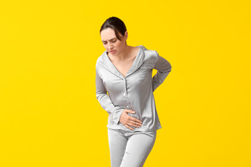 Beautiful young woman suffering from menstrual cramps on yellow background