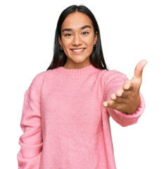 Young asian woman wearing casual winter sweater smiling friendly offering handshake as greeting and welcoming. successful business.