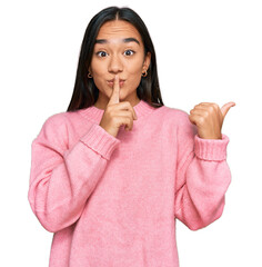 Young asian woman wearing casual winter sweater asking to be quiet with finger on lips pointing...