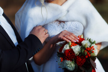 Hands of a newly-married couple with wedding rings on a wedding bouquet of the bride. Bouquet of red and pink roses. Wedding jewelery.