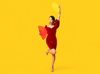 Beautiful young happy Asian woman with fans on yellow background. Chinese New Year celebration - obrazy, fototapety, plakaty