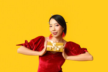 Beautiful young happy Asian woman with gift box on yellow background. Chinese New Year celebration
