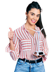 Young hispanic woman holding solar windmill for renewable electricity smiling happy and positive, thumb up doing excellent and approval sign