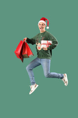 Handsome young happy man with gift boxes and shopping bags jumping on green background