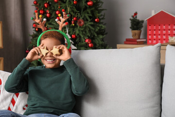 Little African-American boy in reindeer horns with cookies at home on Christmas eve
