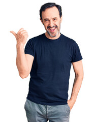 Middle age handsome man wearing casual t-shirt smiling with happy face looking and pointing to the side with thumb up.