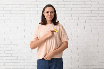 Pretty young woman with yellow ribbon on white brick wall background. Suicide, endometriosis, bone cancer concept