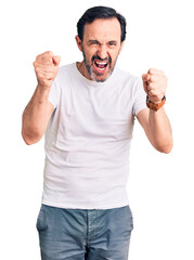 Middle age handsome man wearing casual t-shirt angry and mad raising fists frustrated and furious while shouting with anger. rage and aggressive concept.