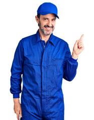 Middle age handsome man wearing mechanic uniform with a big smile on face, pointing with hand finger to the side looking at the camera.
