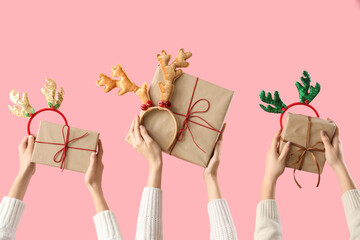 Hands holding Christmas gifts and deer antlers headbands on pink background