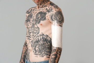 Tattooed man with protective film cover on his arm against grey background