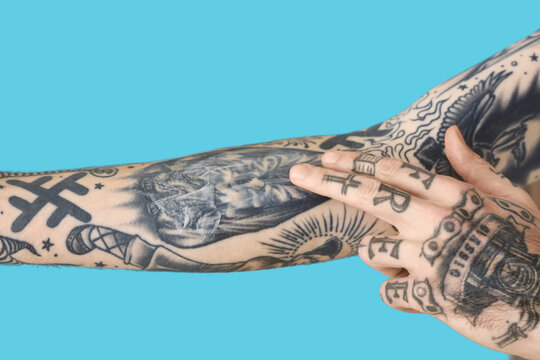 Man applying cream on his arm with tattoos against blue background, closeup
