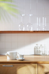 A sunny kitchen with white tile walls, a wooden table and sink.